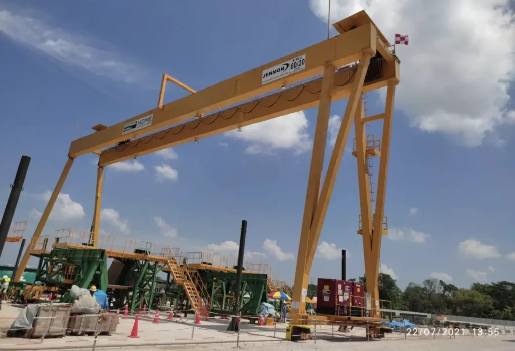 A large yellow gantry crane with a capacity of 60/20 tons at a construction site under a clear blue sky.